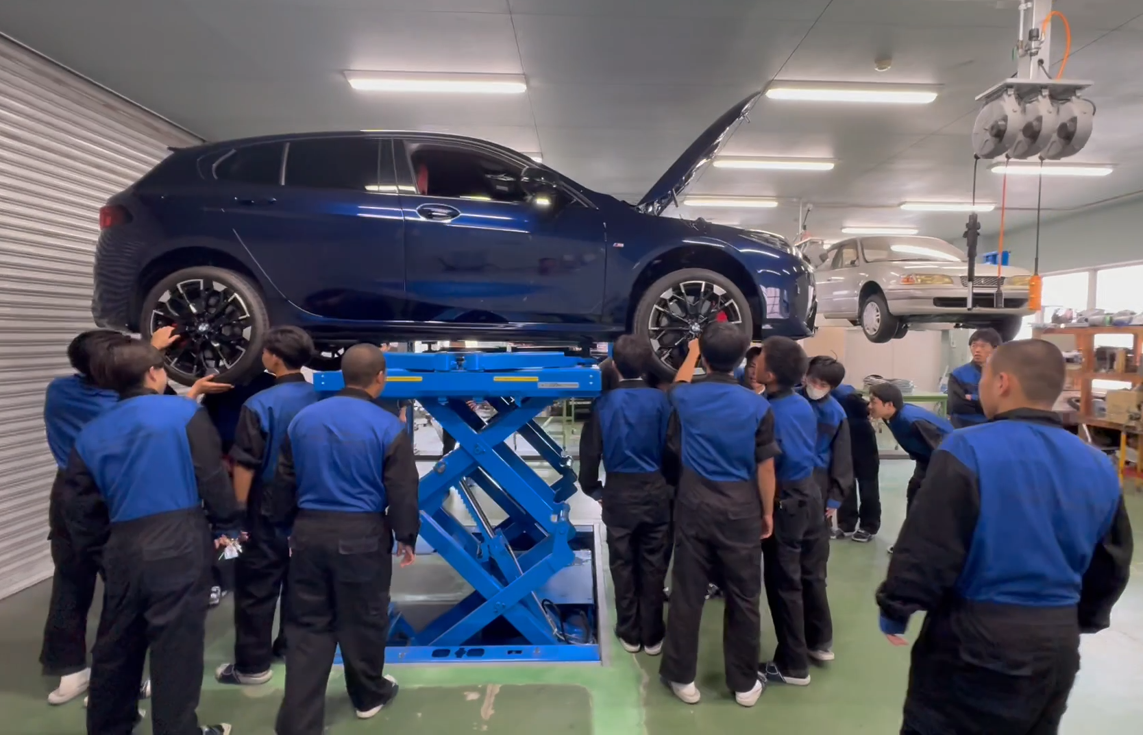 実習棟リフトでBMWの下回りを観察する生徒たち